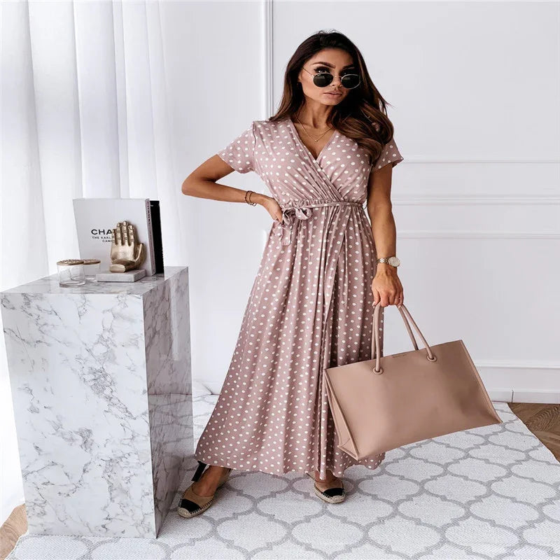 Woman wearing pink polka dot wrap dress with beige tote bag and sunglasses in modern white room