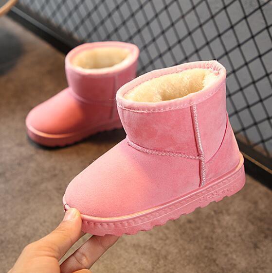 Pair of pink children's winter boots with soft fleece lining on gray floor