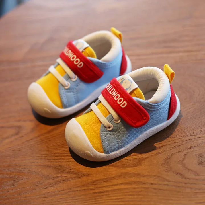 Colorful toddler shoes with yellow, blue, and red design and white soles on wooden surface