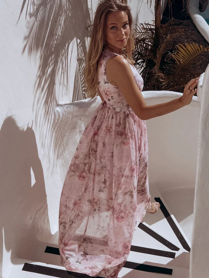 Woman in a pink floral sleeveless maxi dress standing on white stairs with palm shadows