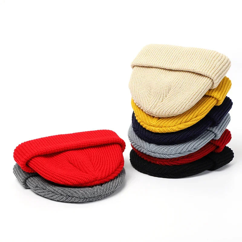 Stack of colorful folded knitted beanies in red, gray, beige, mustard, navy, and black on white background