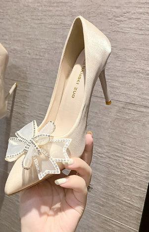Elegant beige high heel shoe with pointed toe and large decorative bow with rhinestones