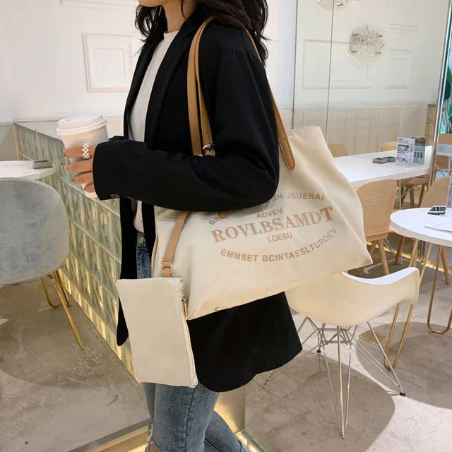 Woman in black blazer holding coffee cup and wearing beige fabric shoulder bag and pouch in modern café