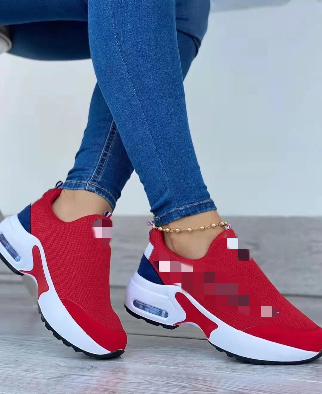 Close-up of person wearing red athletic sneakers with white midsoles and blue accents, paired with blue skinny jeans