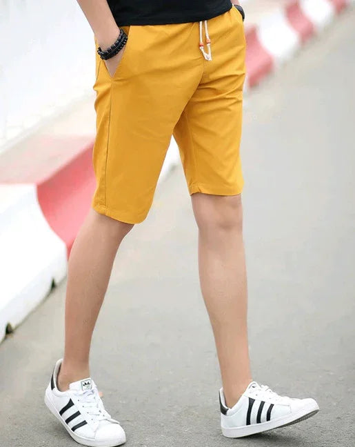 Male model wearing mustard yellow drawstring shorts and white sneakers walking on street