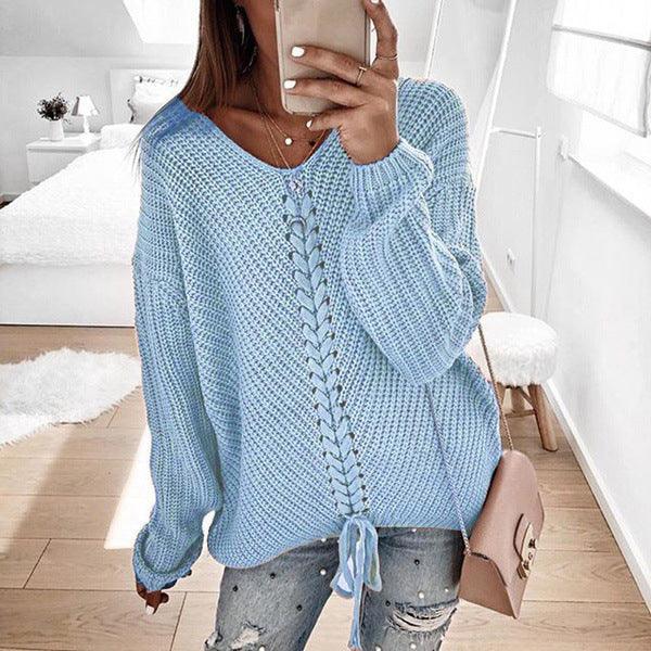 Woman wearing a light blue knit sweater with lace-up front detail, paired with distressed jeans, holding a phone in a bright, modern bedroom