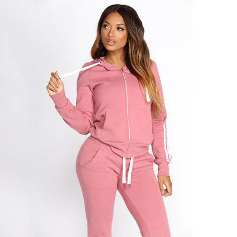 Woman wearing a pink zip-up hoodie and matching jogger pants with white drawstrings and sleeve stripes