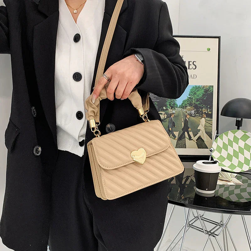 Woman in black blazer holding beige quilted handbag with gold heart clasp near modern office desk