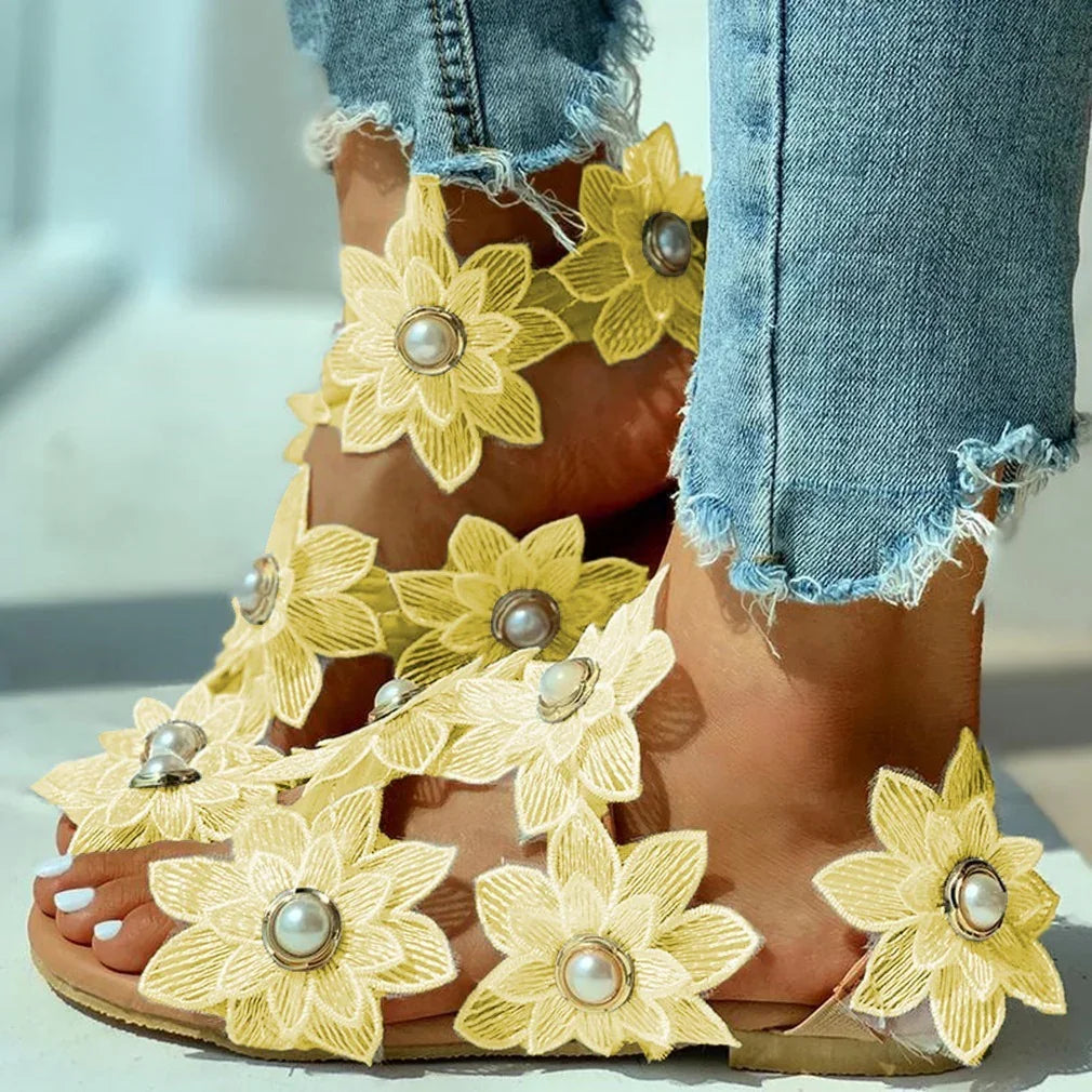 Close-up of feet wearing yellow floral sandals with pearl accents paired with frayed hem blue jeans