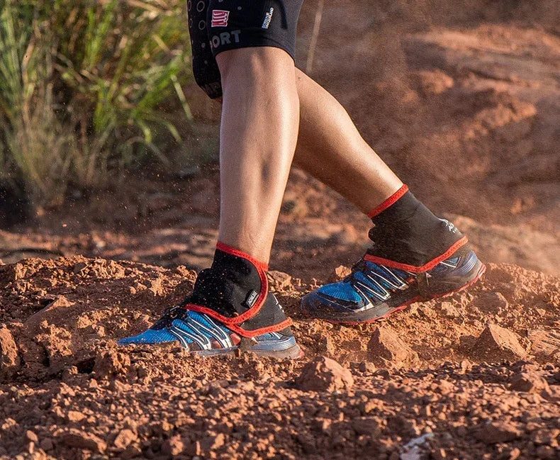 Legs wearing blue trail running shoes and black gaiters on rocky dirt terrain with grass nearby