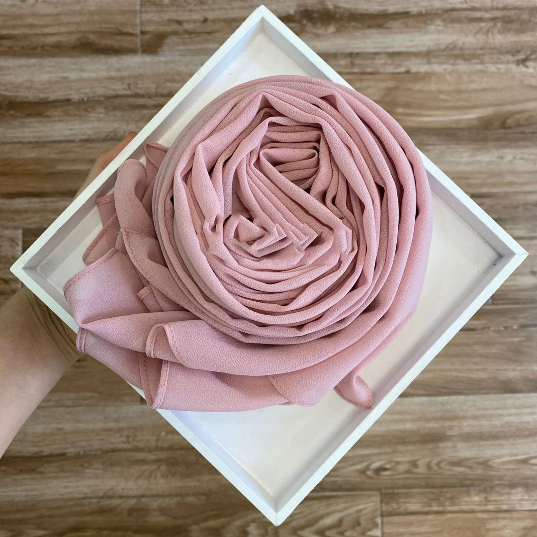 Hand holding white square tray with neatly rolled pink chiffon fabric on wooden floor
