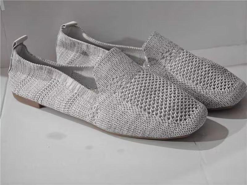 Light gray knitted slip-on loafers with mesh pattern and flat soles on white surface