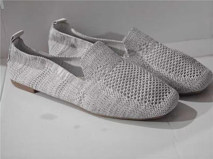 Light gray knitted slip-on loafers with mesh pattern and flat soles on white surface