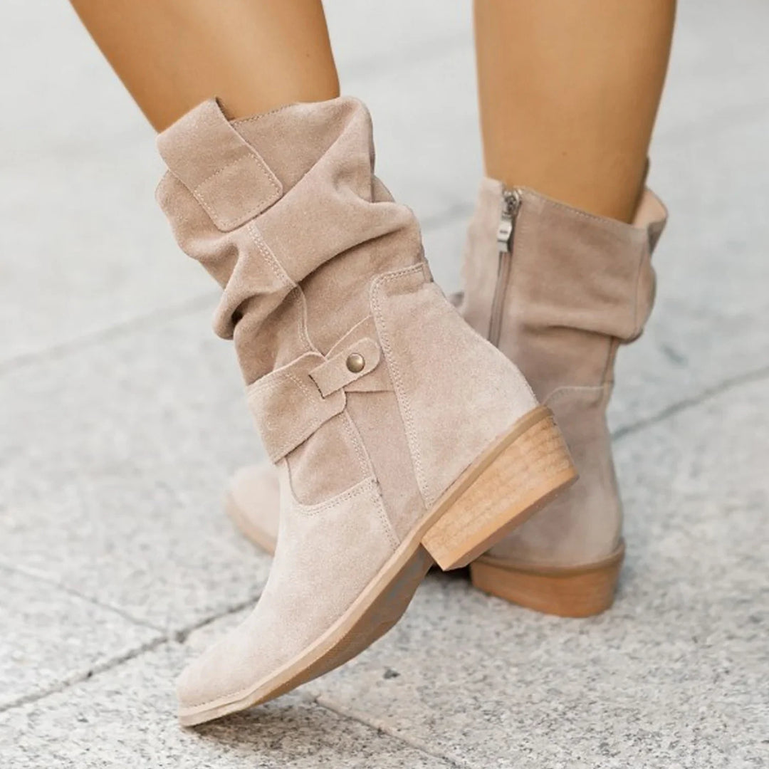 Beige suede ankle boots with stacked wooden heels and side zipper on a stone pavement