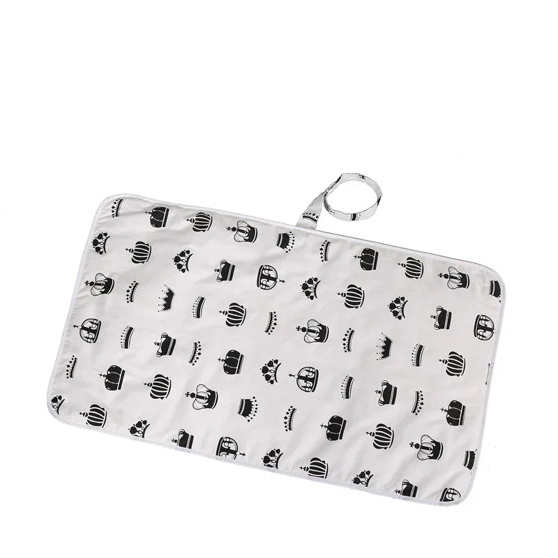 White rectangular changing pad with black crown patterns and carrying strap for baby care