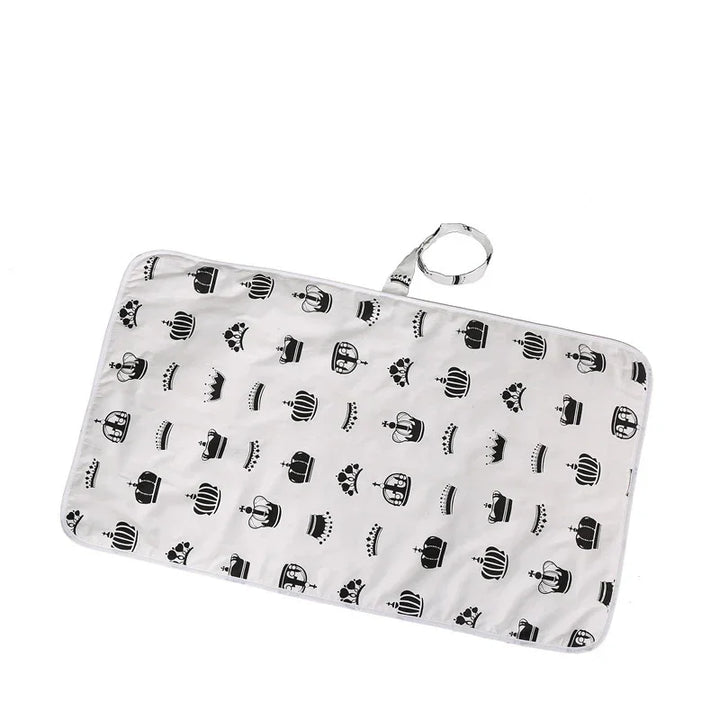 White rectangular changing pad with black crown patterns and carrying strap for baby care