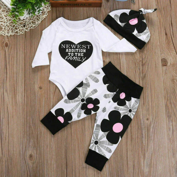 Baby outfit set with white long-sleeve onesie saying 'Newest Addition to the Family', black and white floral pants, and matching hat