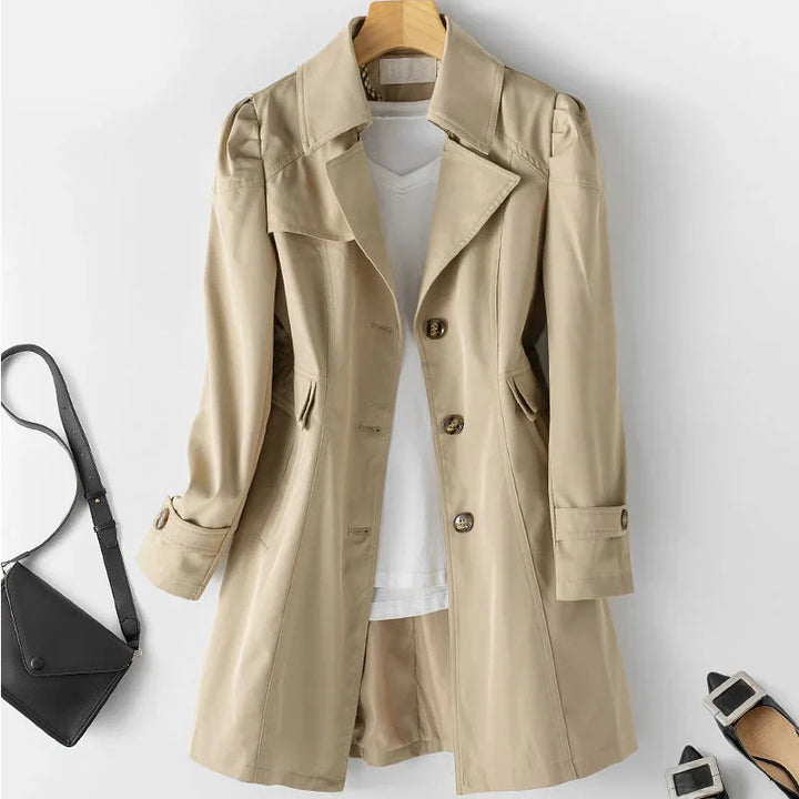 Beige trench coat over white shirt and tan shorts, paired with black crossbody bag and pointed flats