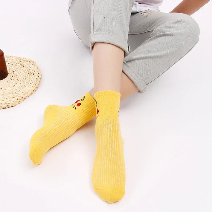Person wearing bright yellow cherry pattern ankle socks with cuffed light gray pants on white background