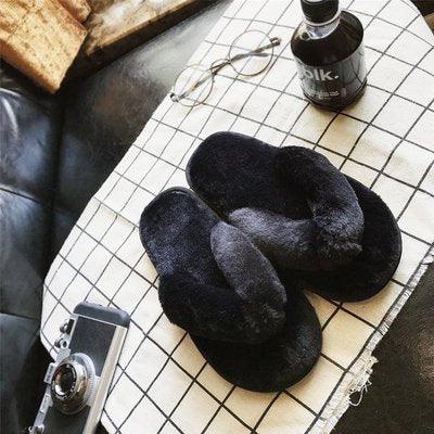 Black furry slippers on a white checkered cloth with a vintage camera and dark bottle nearby