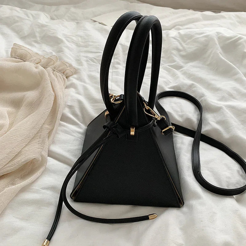 Black triangular leather handbag with double handles and shoulder strap on white fabric