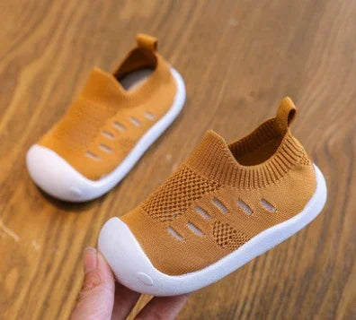 Light brown toddler shoes with breathable knit fabric and white rubber soles on wood floor