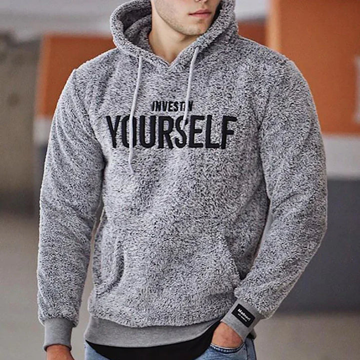 Man wearing gray fuzzy hoodie with black text 'Invest in Yourself' in urban setting