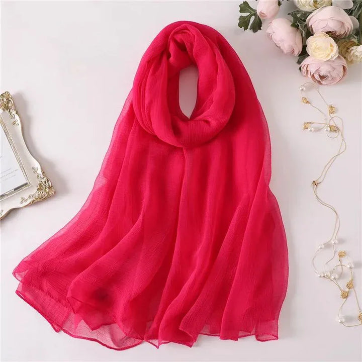 Bright red sheer scarf styled on white surface with pink flowers and pearl jewelry