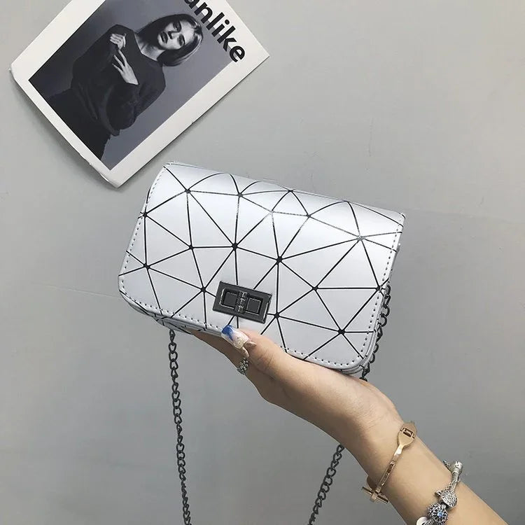 Hand holding a white geometric pattern crossbody bag with a metal chain strap against a gray background