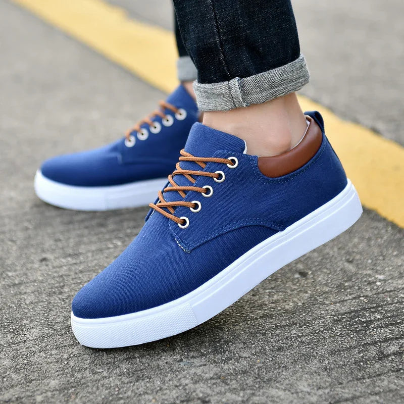 Blue casual sneakers with brown laces and white soles worn with rolled-up dark jeans on pavement