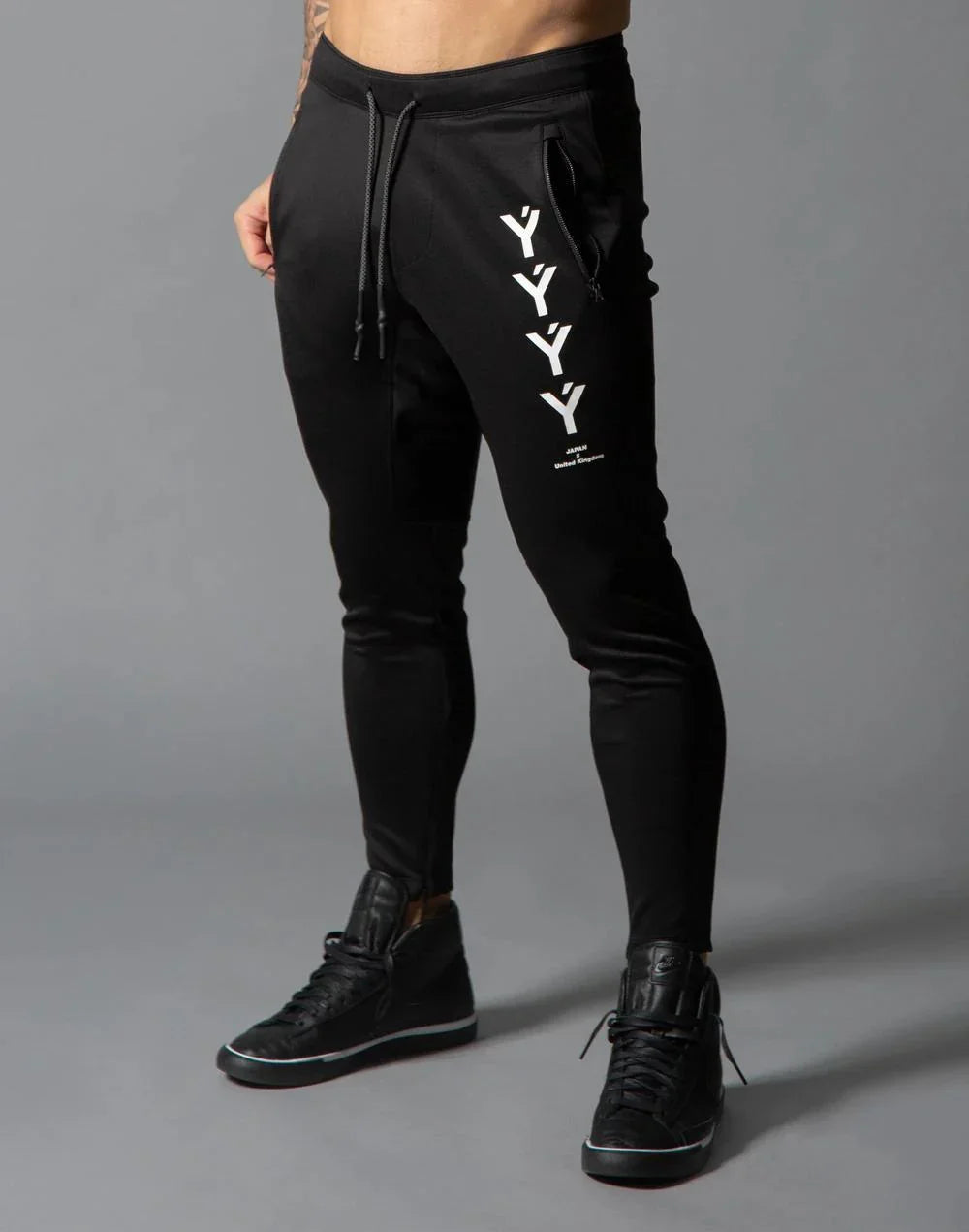 Men's black jogger pants with YYY logo and zippered side pocket, paired with black sneakers