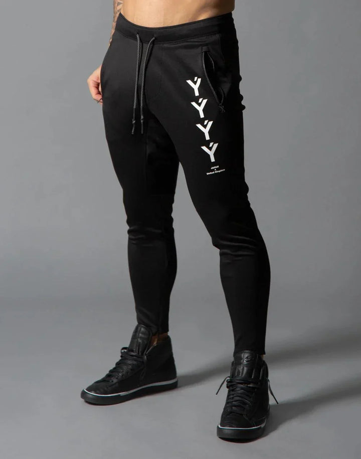 Men's black jogger pants with YYY logo and zippered side pocket, paired with black sneakers