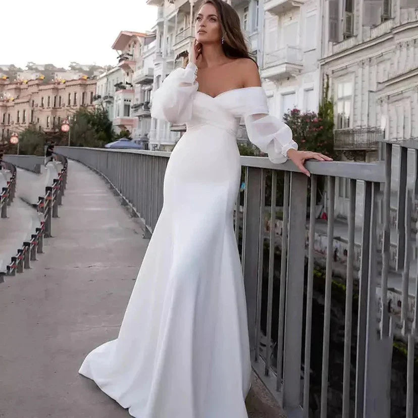 Woman in elegant white off-shoulder wedding gown with puff sleeves standing on city bridge