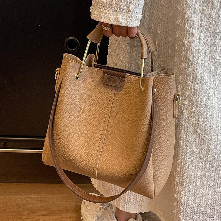 Hand holding a tan leather handbag with gold handles, wearing white textured outfit and sneakers