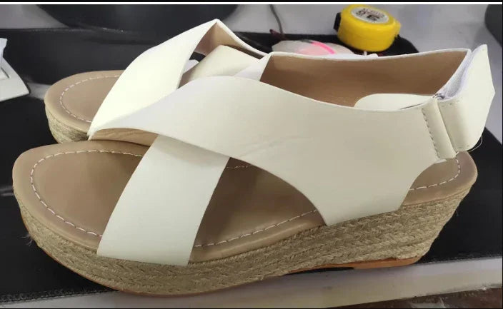 White platform wedge sandals with crisscross straps and jute rope sole on black surface