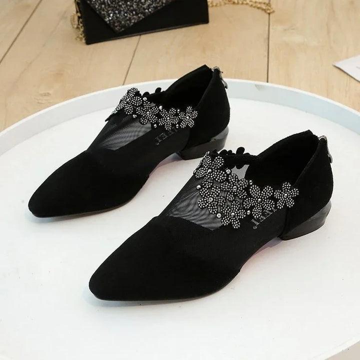 Black pointed-toe women's flats with floral pearl embellishments on mesh upper, displayed on white surface