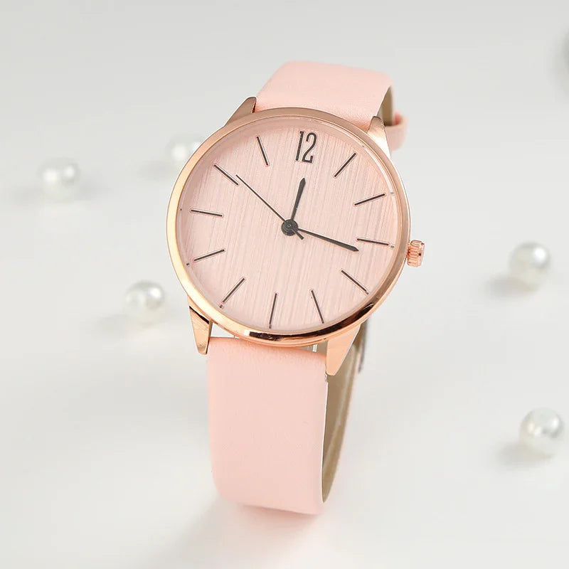 Elegant pink wristwatch with rose gold case and minimalist dial on white background with pearls