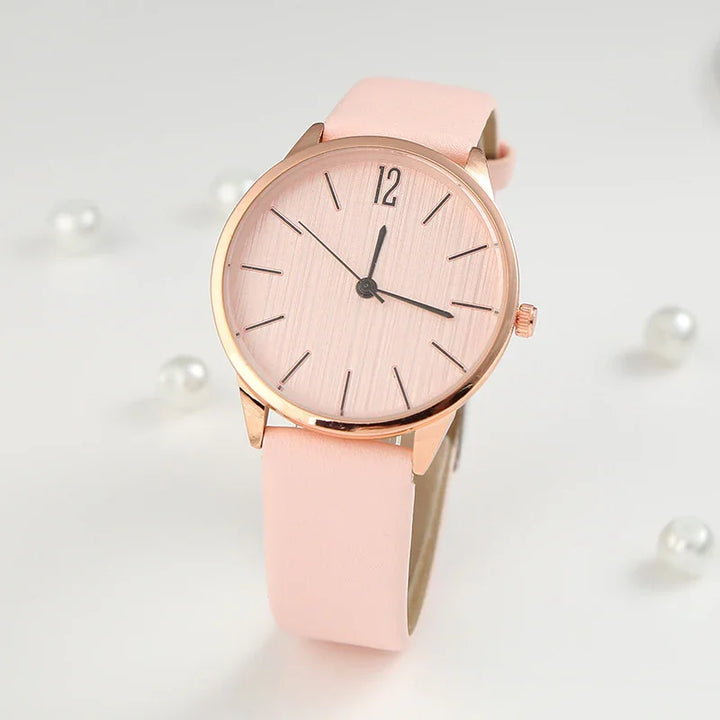Elegant pink wristwatch with rose gold case and minimalist dial on white background with pearls