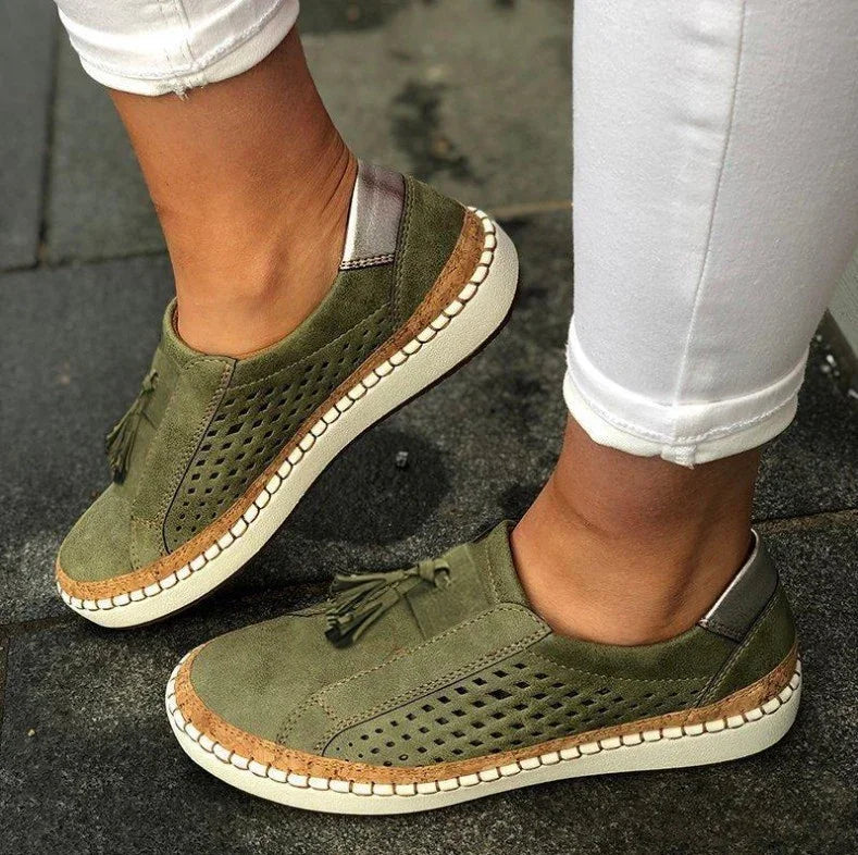 Person wearing olive green suede slip-on sneakers with tassels and white stitched soles on dark pavement