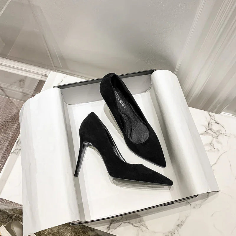 Pair of elegant black suede high heels with pointed toes in an open box on marble floor