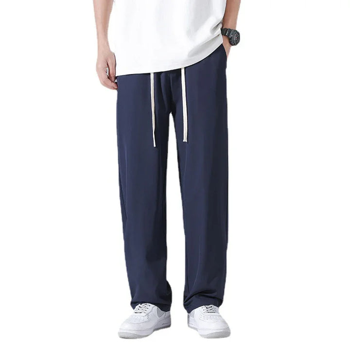 Man wearing navy blue casual pants with white drawstrings, white sneakers, and a white shirt