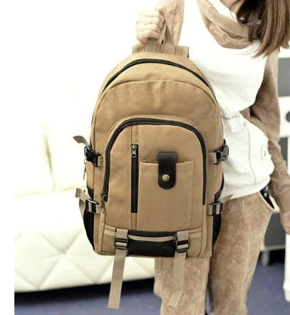 Tan and black canvas backpack with multiple compartments and adjustable straps held by a person indoors