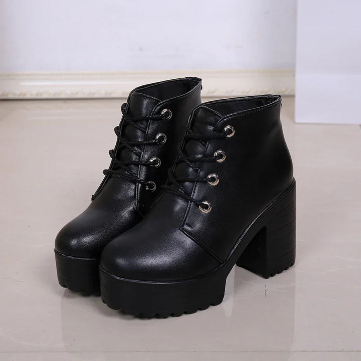 Black leather ankle boots with chunky high heels and lace-up design on a glossy floor
