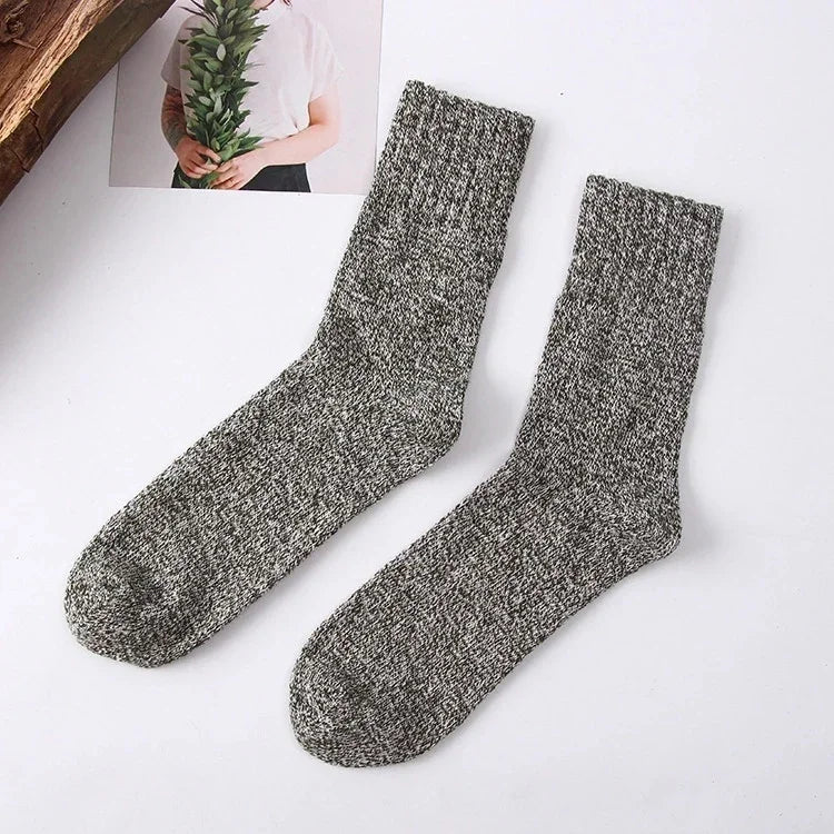 Pair of gray marled knit crew socks on white background with partial view of person holding greenery photo