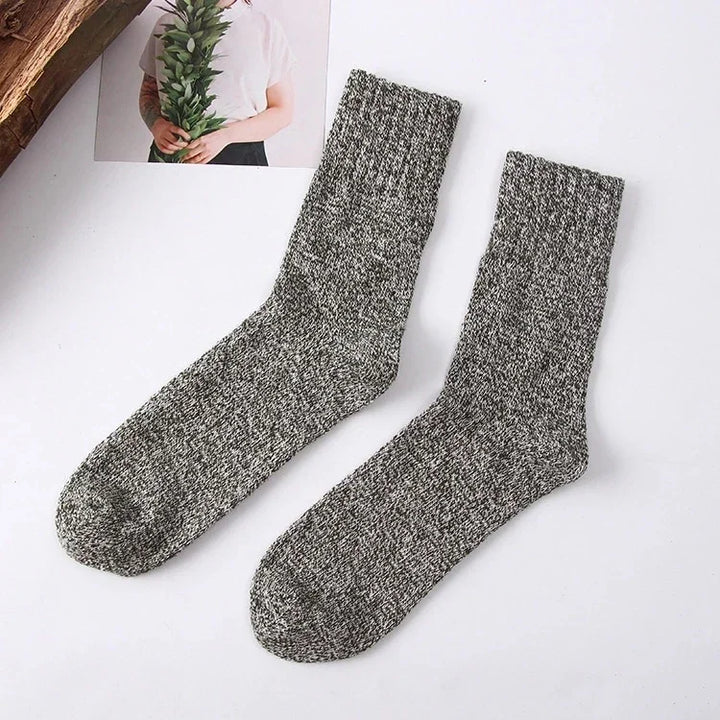 Pair of gray marled knit crew socks on white background with partial view of person holding greenery photo