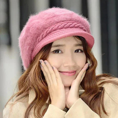 Young woman wearing a soft pink knitted hat and beige coat, smiling gently with hands on cheeks