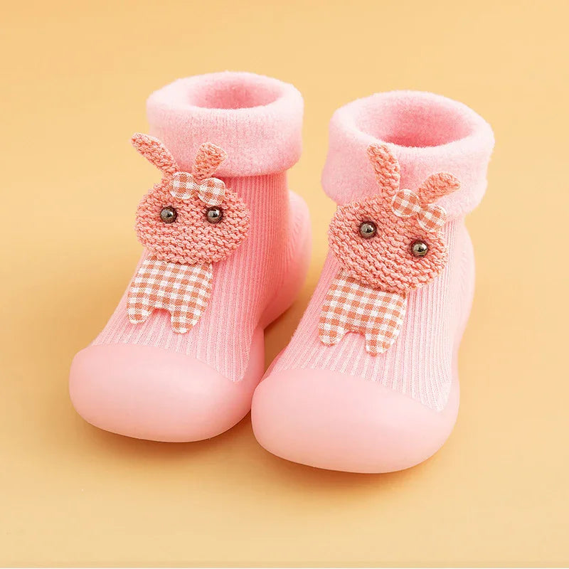 Pair of pink baby socks with soft soles and knitted bunny decorations on a beige background