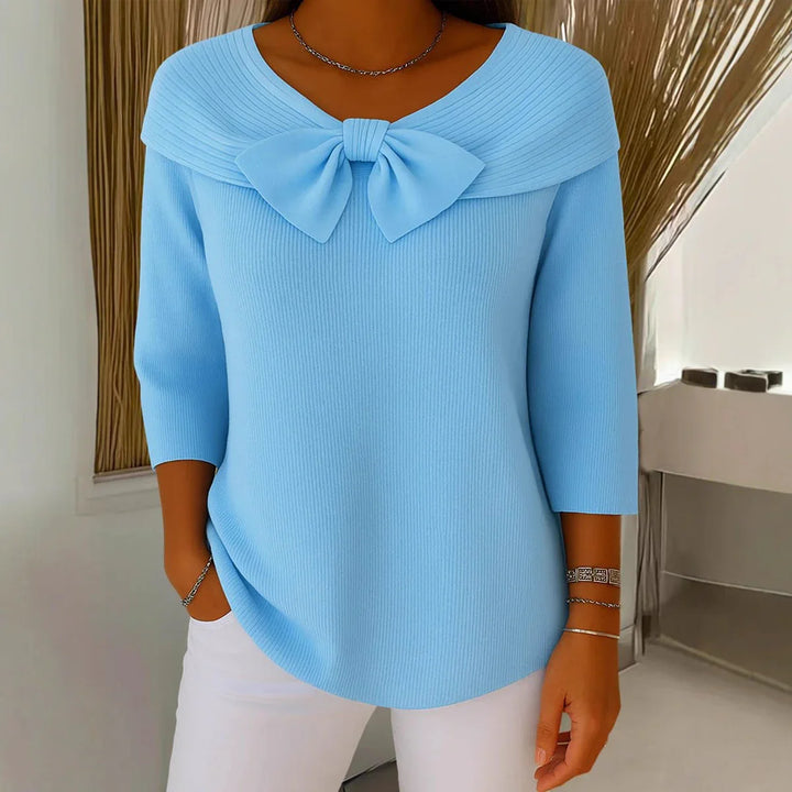 Woman wearing light blue knit sweater with large bow detail and 3/4 sleeves, paired with white pants