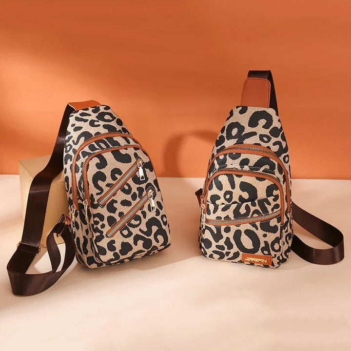 Two leopard print sling bags with brown straps and multiple zippered pockets on beige surface