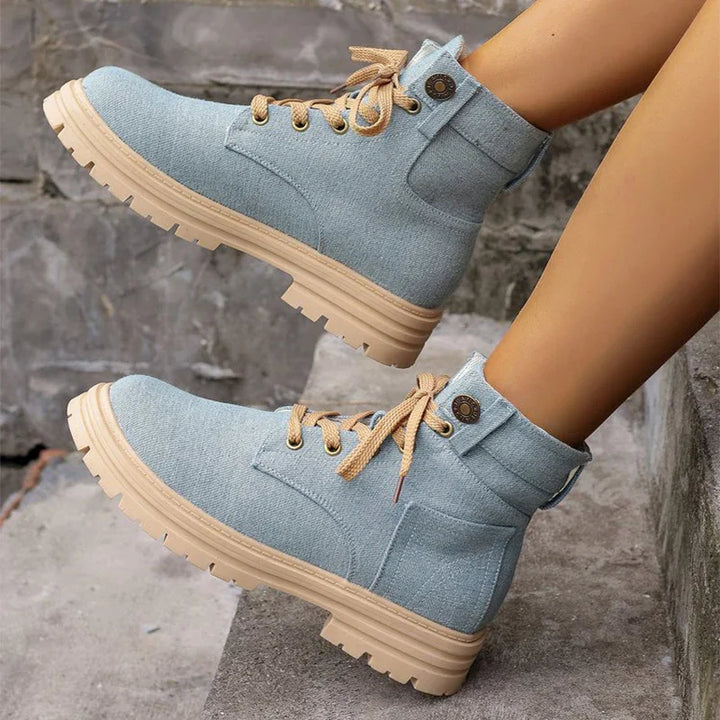 Light blue fabric ankle boots with beige laces and rugged tan soles on concrete steps